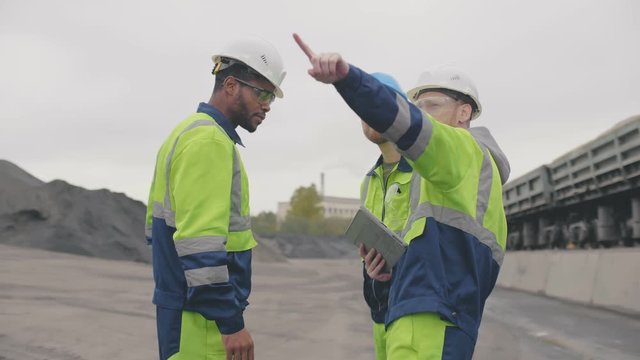 Diverse construction workers or industrial inspectors discuss earthwork at asphalt concrete factory