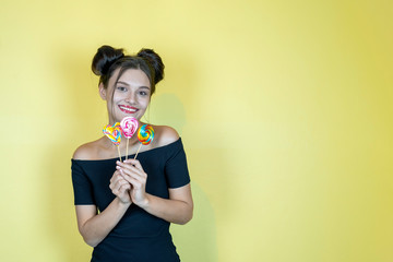 Beautiful happy smiling woman with lollipop and fashion hairstyle on yellow background. Copy space