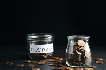 Glass jars with coins and tag BUSINESS on black table