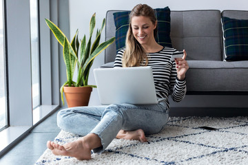 Pretty young woman shopping online with credit card and laptop while sitting on the floor at home.