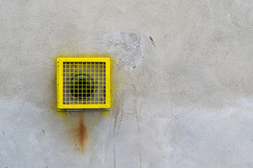 Gas boiler central heating exhaust flue with bright yellow protective metal cage featured buff coloured on a textured wall.