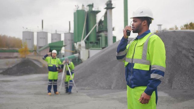 African american geodesist with walkie-talkie at construction site of industrial factory