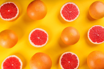 Cut and whole ripe grapefruits on yellow background, flat lay