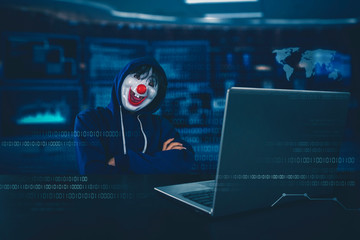 Hacker wearing clown mask with arms folded in a room