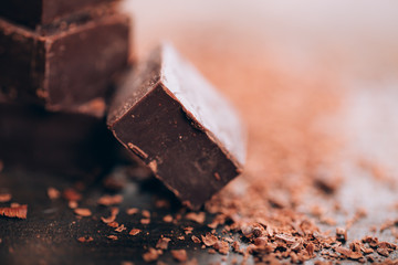 Chopped dark chocolate with cocoa on wooden table, selected focus, close up photo.