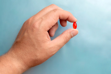 Hand holding red pill on blue background for design. Medical background design. Vitamin, antibiotic pharmaceutical, treatment concept.
