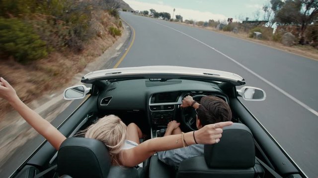 Rear view of couple driving in an open car on highway. Young man and young woman going on road trip with a rental car. 