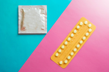 Contraception pills and condom on blue and pink background. Male and female contraceptives concept. Bitrh control concept.