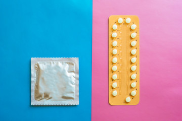 Contraception pills and condom on blue and pink background. Male and female contraceptives concept. Bitrh control concept.