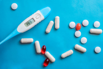 Thermometer showing high body temperaturep and pills on blue background. Flu cold concept. Healthcare medical concept. Medicine pill. Emergency medical treatment. Disease treatment.