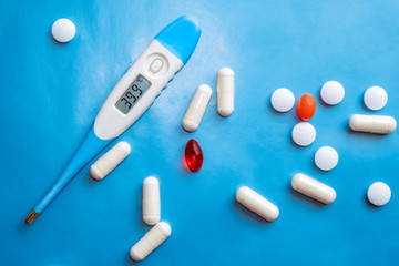 Thermometer showing high body temperaturep and pills on blue background. Flu cold concept. Healthcare medical concept. Medicine pill. Emergency medical treatment. Disease treatment.