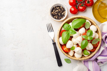 Traditional Italian caprese salad with mozzarella cheese, cherry tomatoes and basil in ceramic bowl on concrete background. Top view, copy space.