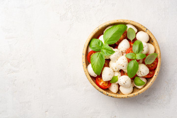 Traditional Italian caprese salad with mozzarella cheese, cherry tomatoes and basil in ceramic bowl on concrete background. Top view, copy space.