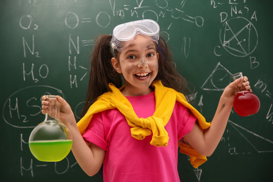 Schoolgirl holding flasks near chalkboard with chemical formulas