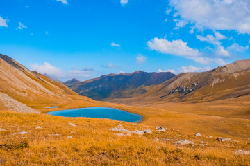 Mountain moraine lake in autumn with blue cloudy sky. Beautiful scenic view. Tranquil background, sunlight. Idyllic scenery. Beautiful alpine landscape. Mountain hiking.