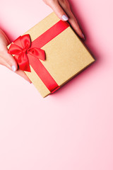 Woman holding red and golden gift box on pastel pink background with heart shape confetti, copyspace. Valentine's Day, Women's Day or Mother's Day greeting card in trendy colors