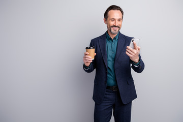 Photo of handsome friendly business man chief hold telephone hands read corporate email drink hot coffee to go formalwear blazer shirt trousers blue suit isolated grey color background
