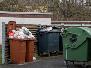 Garbage bins in different colors filled to overflowing as sign for an affluent society