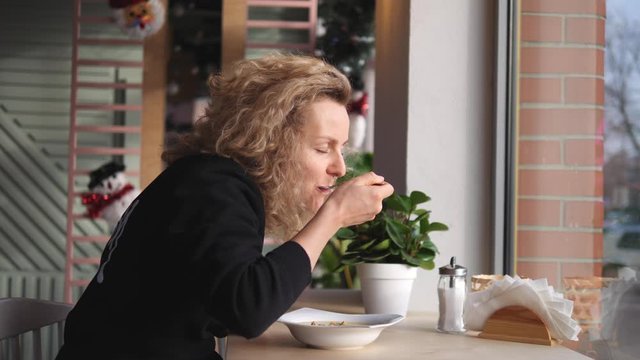 Young Curly Woman Eating Cream Soup In Cafe