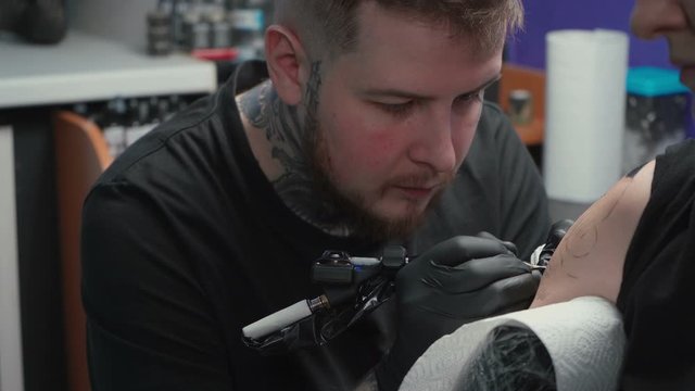 Footage of man doing dark tattoo of snake for woman in studio