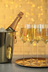 Glasses of champagne and ice bucket with bottle on grey table