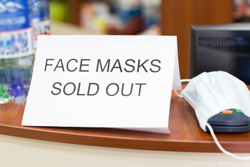 Information plate on counter in pharmacy with text: face masks are sold out, not in stock. Epidemic of N-CoV 2019 influenza coronavirus mutated and spreading in China. Bank card payment terminal