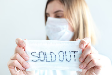 Woman in disposable blue medical shirt holds in hands information plate with text: face masks are out of stock, sold out. Epidemic of N-CoV 2019 influenza coronavirus mutated and spreading in China