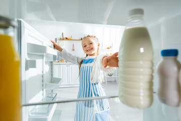 selective focus of smiling kid taking bottle with milk from fridge