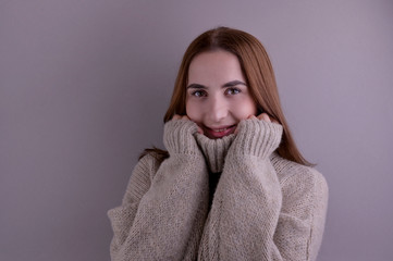 Beautiful smiling girl in a sweater on a gray background. Studio shot. Modern portrait. Copy space.
