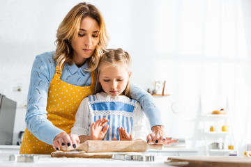 attractive mother and daughter rolling dough on cutting board