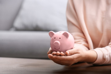 Woman with piggy bank at wooden table, closeup. Space for text