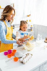 mother and daughter in aprons mixing dough in kitchen