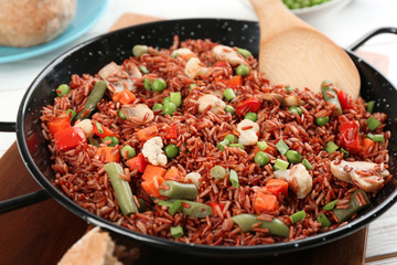 Tasty brown rice with vegetables on white wooden table, closeup