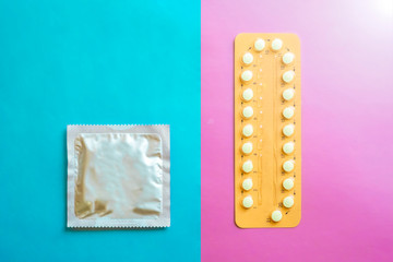 Contraception pills and condom on blue and pink background. Male and female contraceptives concept. Bitrh control concept.