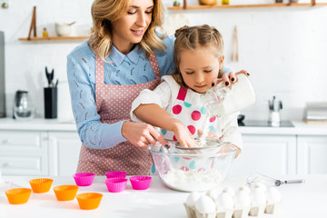Beautiful mother and cute daughter sifting flour through sieve into bowl