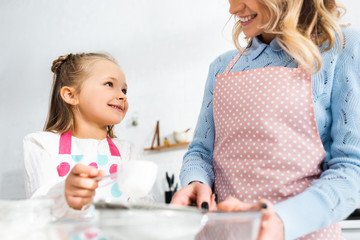 cropped view of mother looking at cute daughter in kitchen