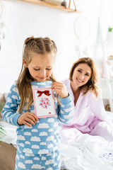 selective focus of daughter holding card and smiling mother on background in international womens day