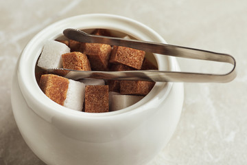 Different refined sugar cubes in bowl on light table, closeup