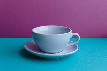 Blue cup and saucer on a pink and blue background side view.