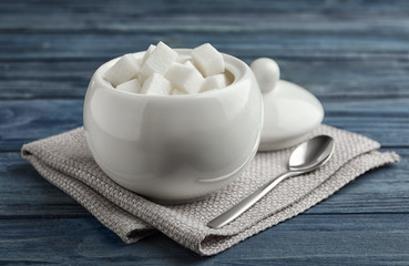 Refined sugar cubes in ceramic bowl on blue wooden table