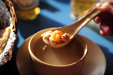 Hand holding a spoon with a shrimp and a piece of boiled fish, close-up. Seafood soup at the beach...
