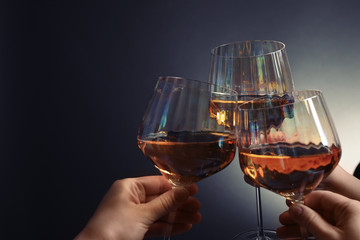 Women clinking glasses with white wine on dark background, closeup