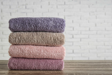 Stack of clean bath towels on wooden table near white brick wall. Space for text
