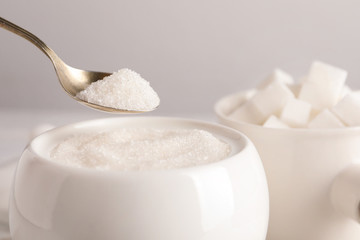 Taking spoon of white sugar from ceramic bowl on table, closeup