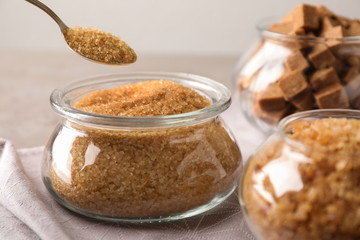 Taking spoon of brown sugar from glass bowl on table