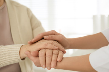 Doctor holding senior patient's hands in office , closeup