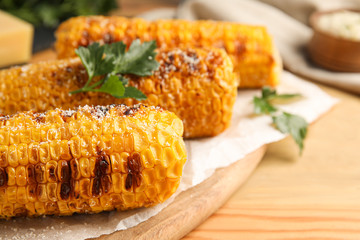 Delicious grilled corn cobs on wooden table, closeup
