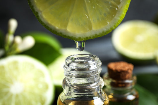 Citrus essential oil dripping from lime slice into bottle, closeup