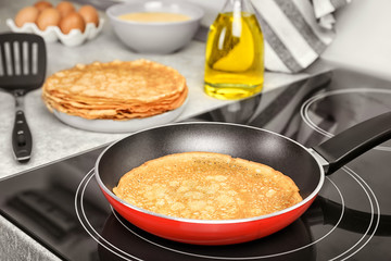 Delicious thin pancake in frying pan on induction stove, closeup