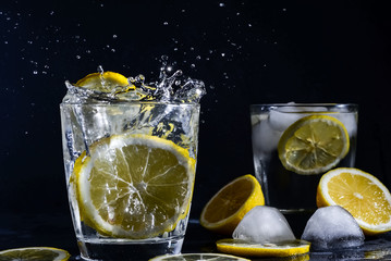  splash Gin and tonic cocktail with lemon slices Ice cube falls into water with lemon Copy space,...